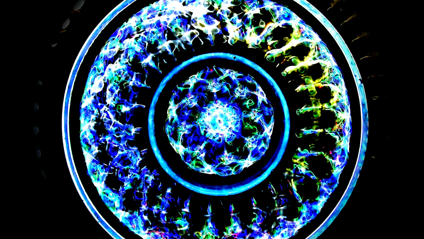 Cymatics standing wave pattern at 23.49Hz — turbulent core framed by electric blue rings
