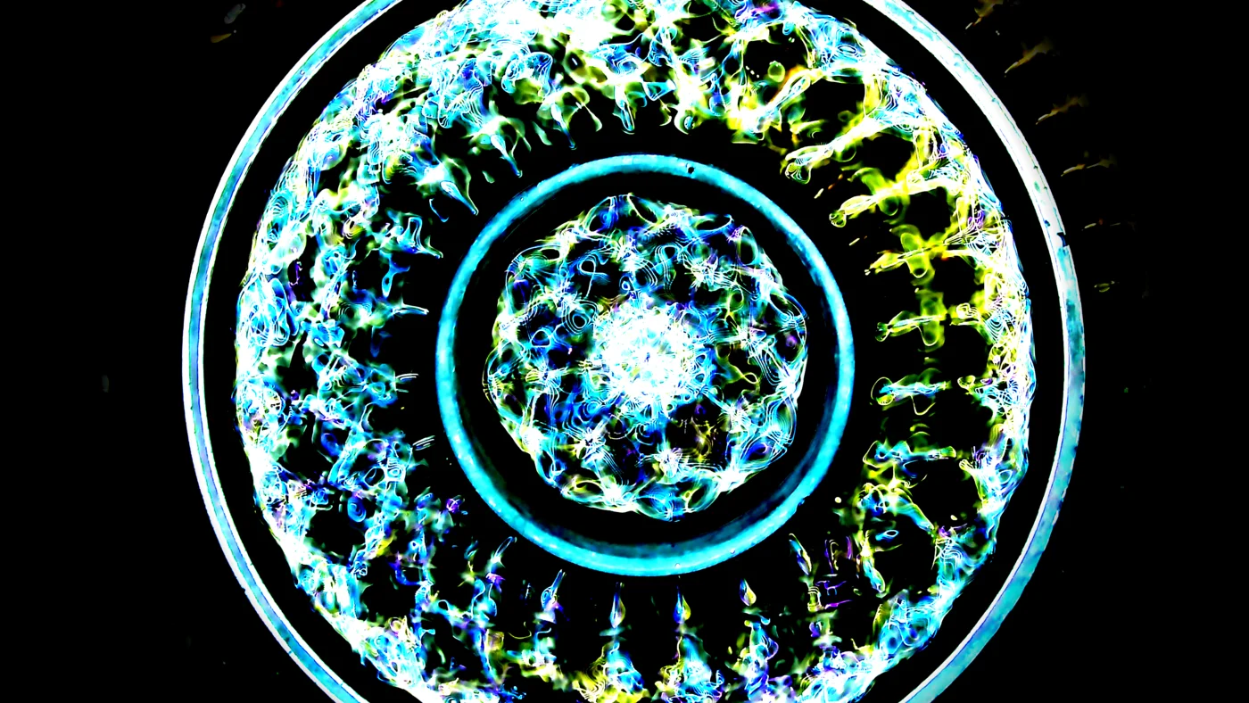 Cymatics standing wave pattern at 23.49Hz — fine lace-like lattice detail with blue-green-yellow color balance